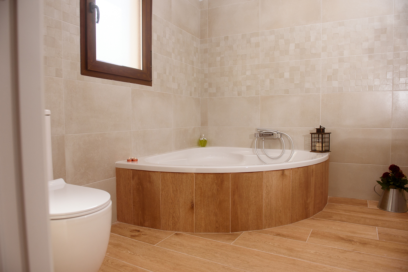 Baño principal con bañera de esquina, azulejos beige y ventana con luz natural