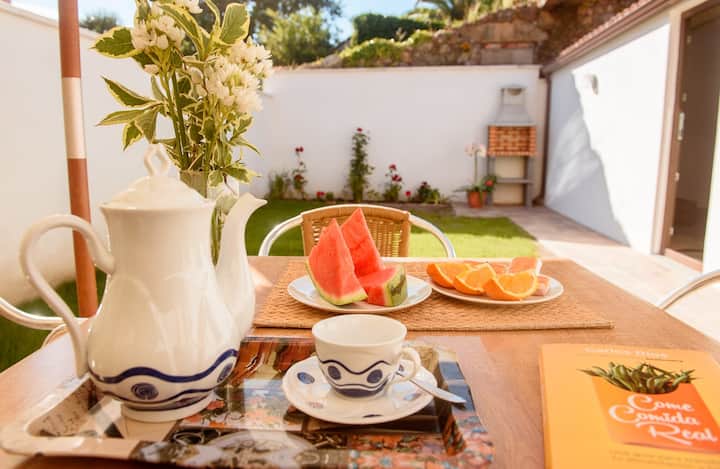 Desayuno en la terraza de Casa Brétema con café, sandía y naranjas frescas, y el jardín privado al fondo