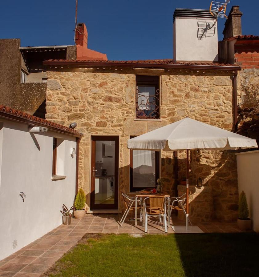 Vista exterior de la fachada de piedra de Casa Brétema con terraza, mesa, sombrilla y jardín