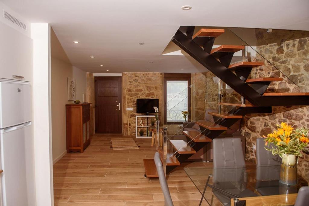 Vista del salón con la escalera industrial de madera y cristal, frigorífico y pared de piedra al fondo