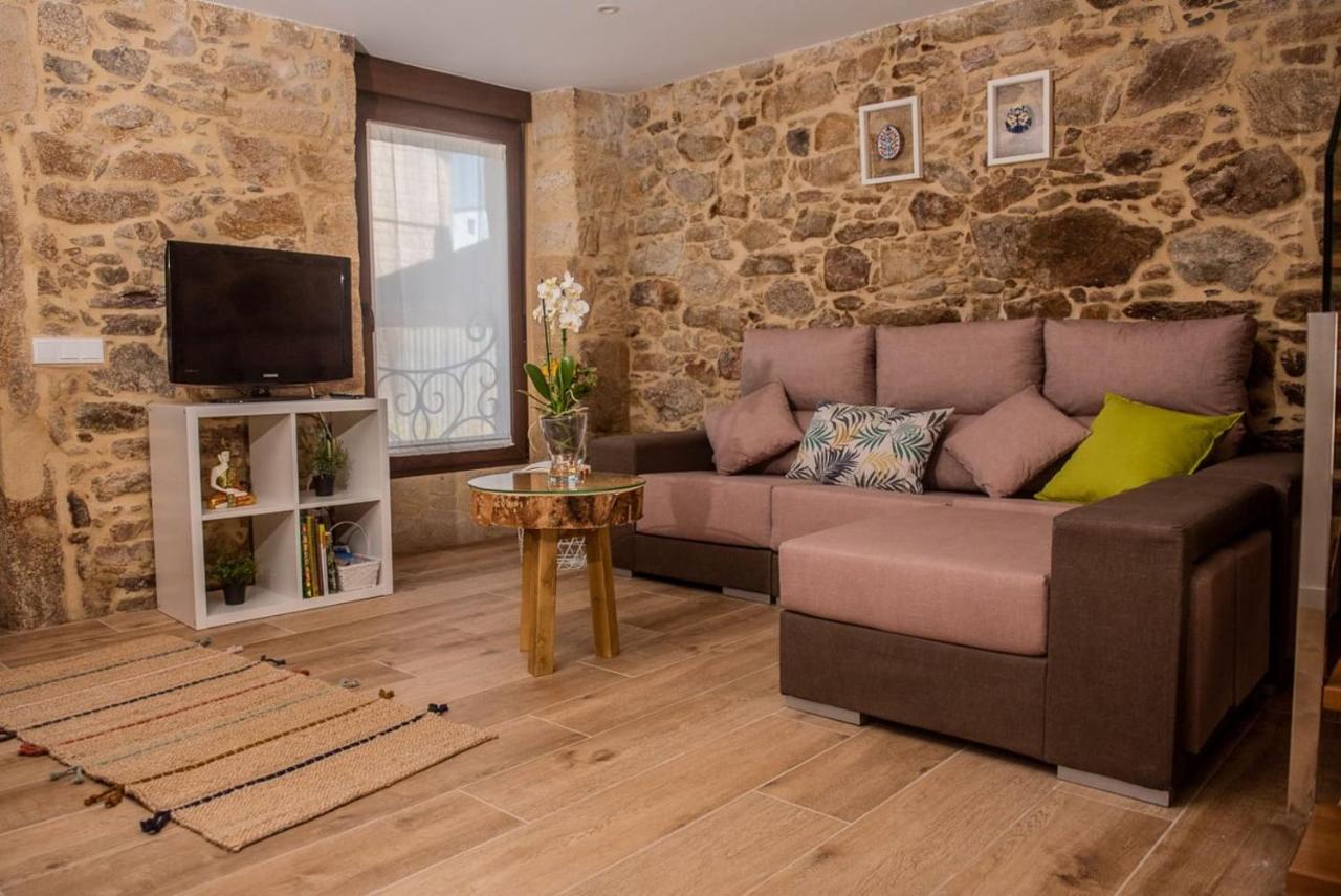 Salón de Casa Brétema con sofá amplio, televisión y pared de piedra gallega original